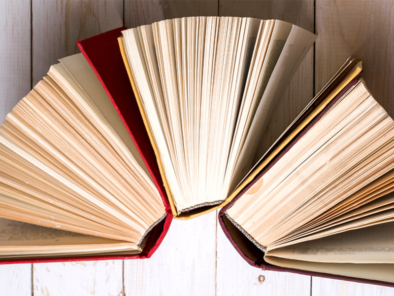 Mehrere aufgeschlagene Bücher liegen fächerförmig auf einem Holztisch.