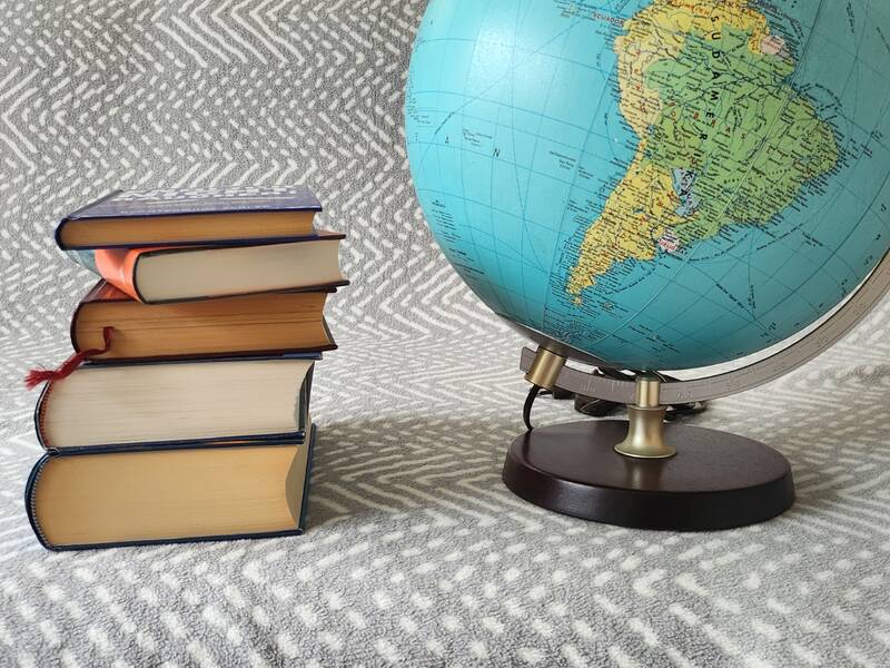 Ein Stapel Bücher liegt neben einem Globus auf einer gemusterten Unterlage.