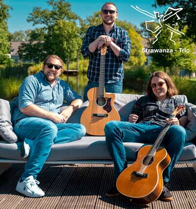 Das Bild zeigt das Strawanza Trio, auf einem Sofa sitzend oder stehend, jeder mit einer Gitarre in der Hand, in einer sonnigen, grünen Parklandschaft.