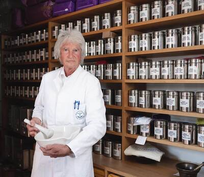Dr. Günther Fleischmann steht vor dem Apothekenregal und hält einen Mörser und Stößel in den Händen.