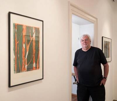 Ernst Geyer steht in einem Türrahmen eines weißen Raumes, an dessen Wänden mehrere gerahmte abstrakte Kunstwerke hängen.