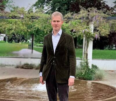 Peter Prinz von Lobkowicz steht draußen vor einem Brunnen, umgeben von Bäumen und Grünflächen.