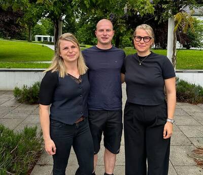 Nina, Jakob und Lisa Tomschiczek stehen auf einem gepflasterten Weg vor einer grünen Rasenfläche mit Bäumen im Hintergrund