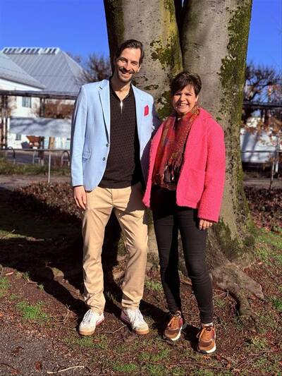Podcast-Moderator Johann Struck und Irene Holzapfel stehen lächelnd gemeinsam vor einem großen Baum.