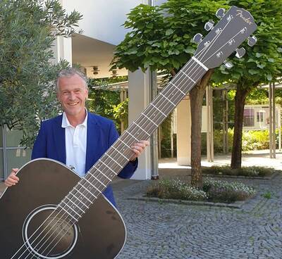 Augustin Wiedemann hält vor dem Kurpark eine überdimensionale Konzert-Gitarre in seinen Händen