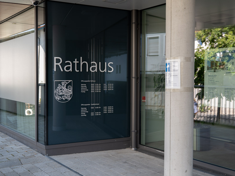 Seitlicher Eingang des Rathauses Bad Aibling. Blick auf die Öffnungszeiten.