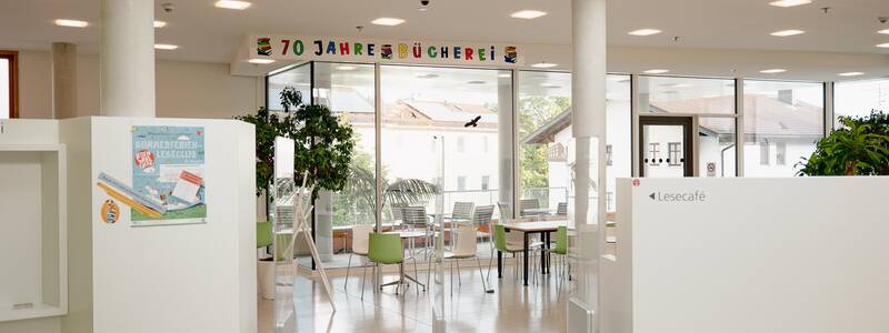 Ein modernes Lesecafé mit großen Fenstern, dekoriert mit dem Schriftzug "70 Jahre Bücherei", und im Hintergrund stehen Tische und Stühle.