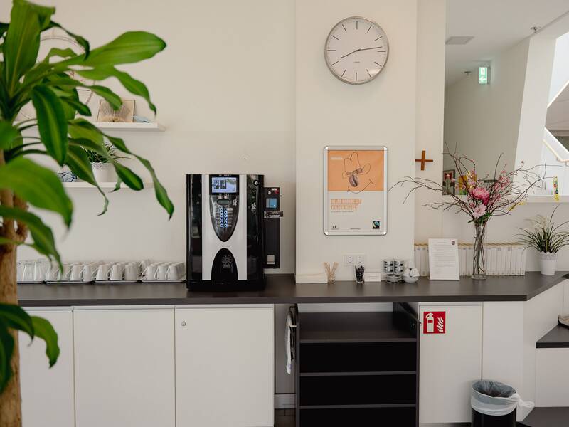 Ein Aufenthaltsraum mit einem Kaffeeautomaten, einer Uhr, dekorativen Pflanzen und Tassen auf einer Theke.