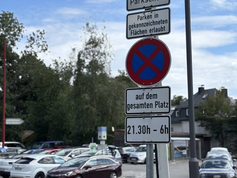 Ein Parkplatz mit mehreren Autos und einem Schild, das das Parken mit Parkschein auf gekennzeichneten Flächen erlaubt und ein Halteverbot von 21:30 Uhr bis 6:00 Uhr anzeigt.