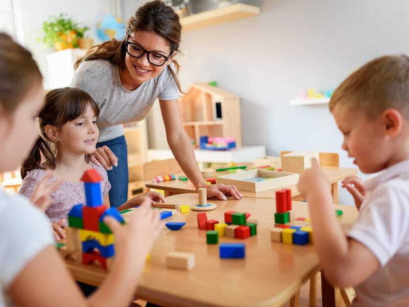 Erzieherin spielt mit Kindern an einem Tisch.